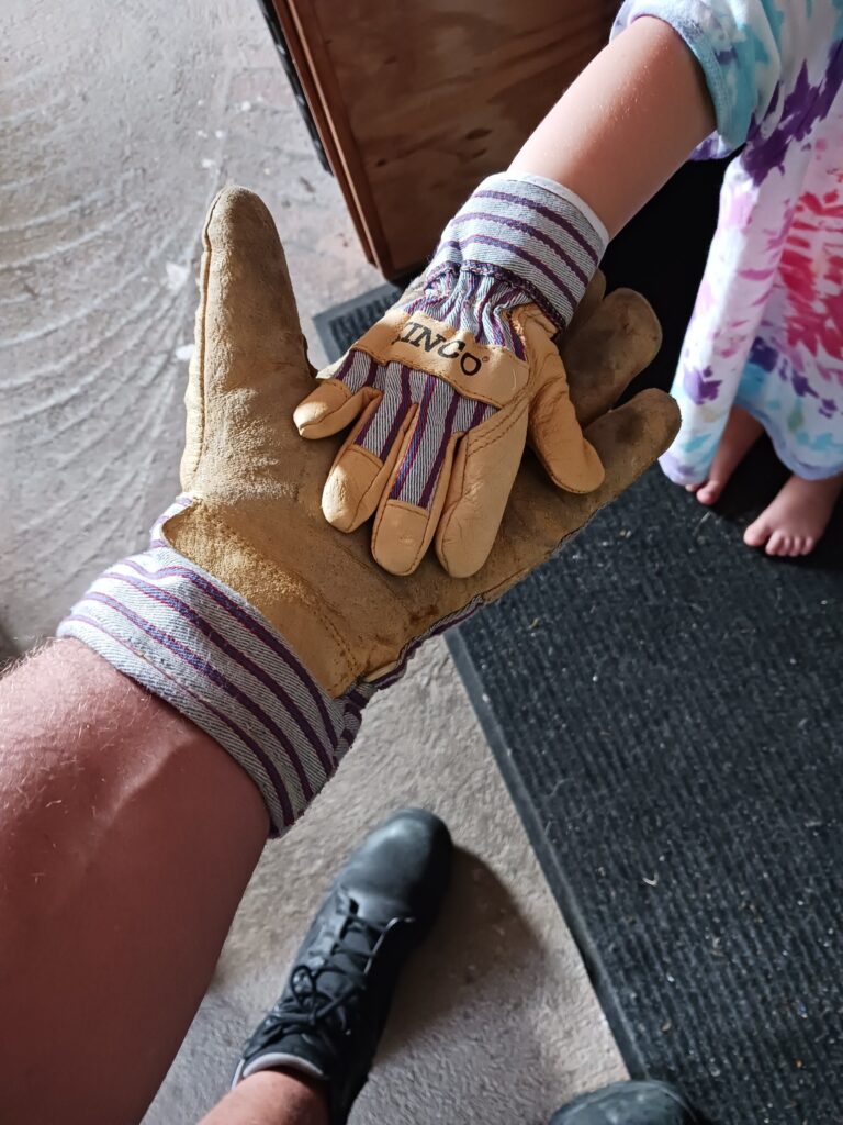 Small childs hand in a tiny work glove laying in the palm of an adult mans gloved hand
